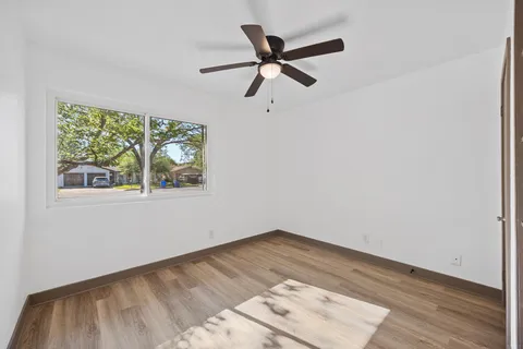 a view of an empty room with wooden floor and a ceiling fan