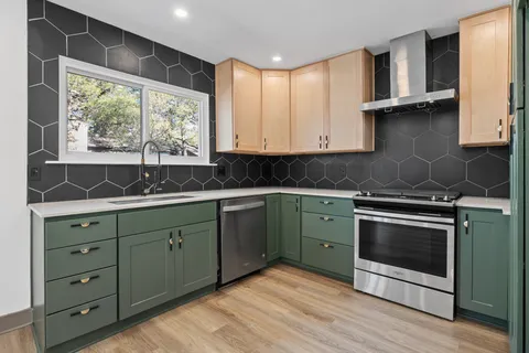 a large kitchen with kitchen island a large window a sink stainless steel appliances and cabinets