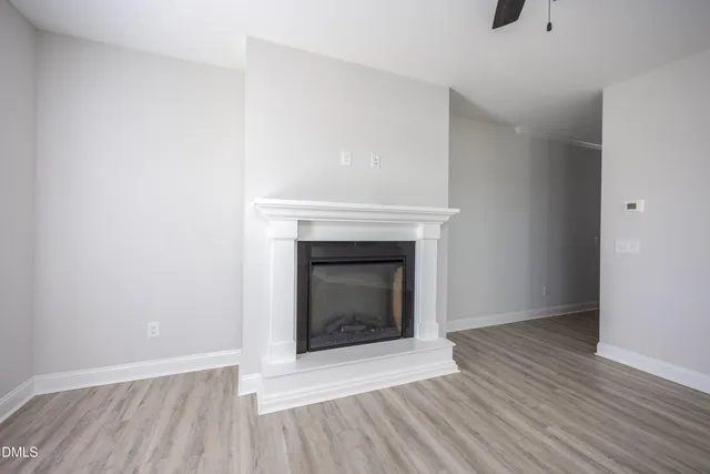 an empty room with wooden floor a ceiling fan a fireplace and windows