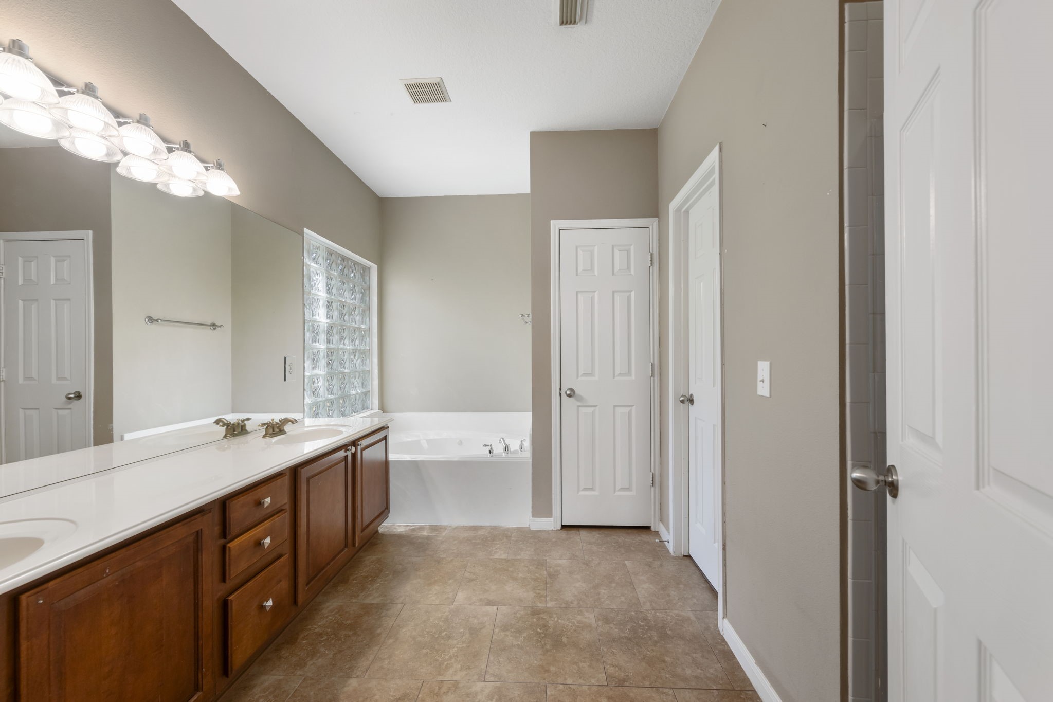 2907 Stemwood Drive Spring, TX 77388 - Photo 15 of 33 Spacious primary bath featuring dual vanities, ample cabinet storage, a soaking tub framed by glass block windows, and a bright, open layout designed for comfort and functionality.