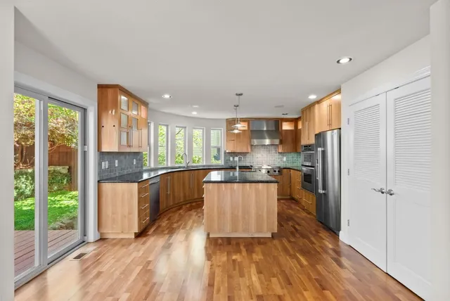 a kitchen with stainless steel appliances granite countertop a refrigerator a oven a sink and white cabinets with wooden floor