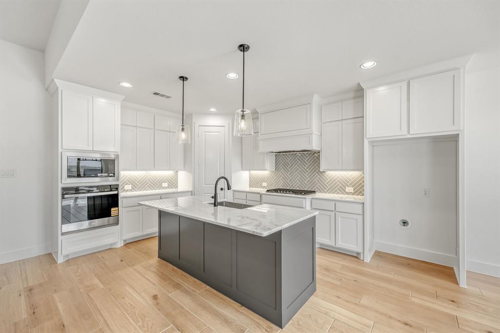 147 Derrett Lane Rhome, TX 76078 - Photo 5 of 28 Kitchen featuring two tone cabinets, stainless steel appliances, an island with sink, hanging light fixtures, and backsplash