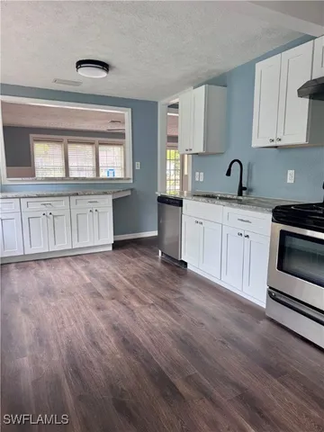 a kitchen with granite countertop white cabinets a sink and dishwasher with wooden floor