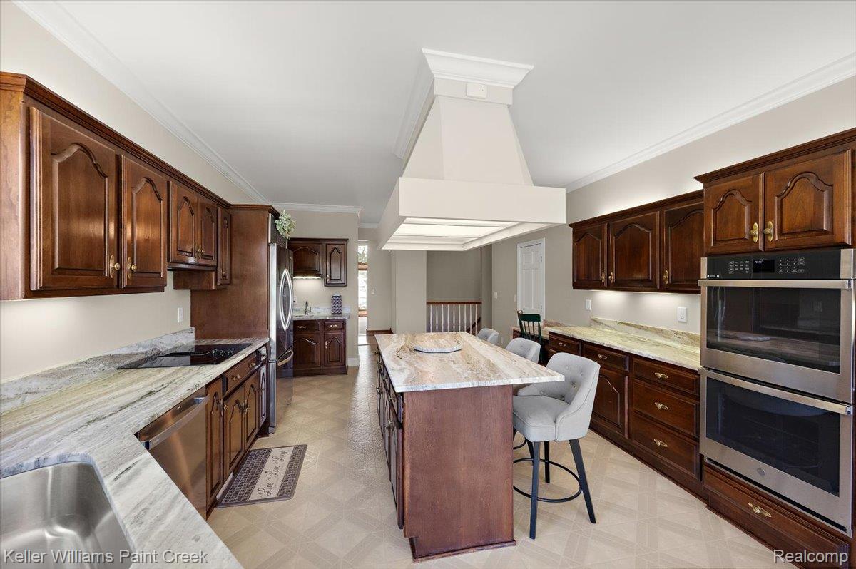 69069 Campground Road Romeo, MI 48065 - Photo 33 of 78 Spacious kitchen featuring rich wood cabinetry, stone countertops, stainless steel appliances, a large center island with seating, and integrated ceiling lighting