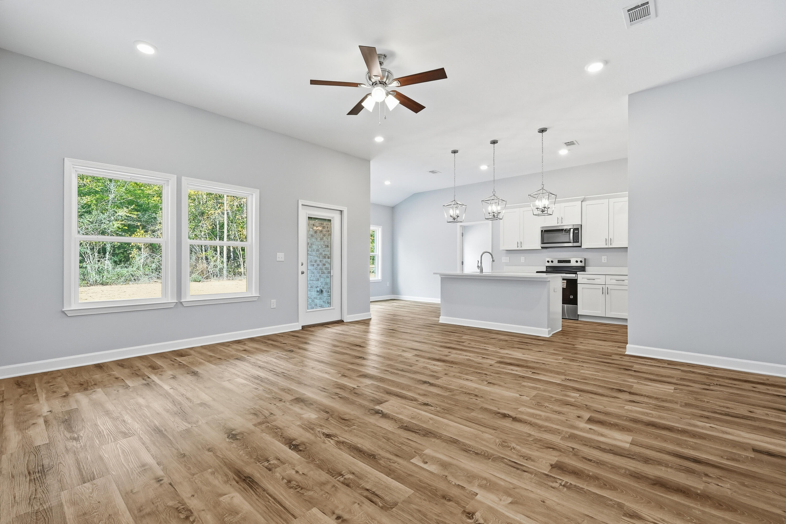 6104 Mildred's Way Crestview, FL 32539 - Photo 4 of 23 an empty room with wooden floor a ceiling fan and kitchen view