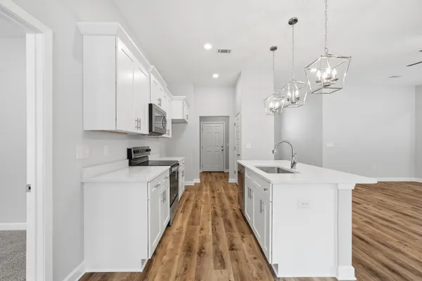 a spacious kitchen with stainless steel appliances granite countertop a sink dishwasher a stove and white cabinets with wooden floor