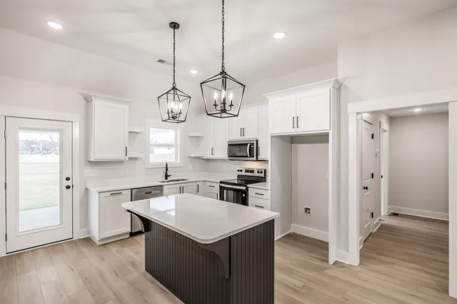 a kitchen with a refrigerator a sink dishwasher a kitchen island with wooden floor and cabinets