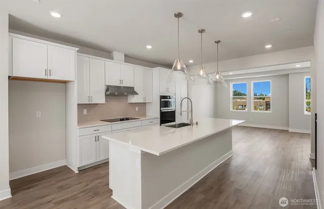 a kitchen with kitchen island a stove a sink a refrigerator and white cabinets with wooden floor