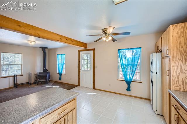 365 Alpine View Road Divide, CO 80814 - Photo 26 of 26 Kitchen with a wealth of natural light, beamed ceiling, a wood stove, white refrigerator, and light brown cabinets