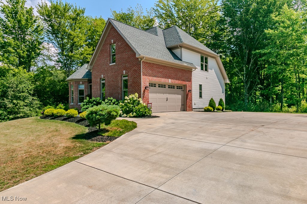 8675 Auburn Road Chardon, OH 44024 - Photo 5 of 35 View of property exterior featuring brick siding, concrete driveway, a shingled roof, a yard, and view of wooded area
