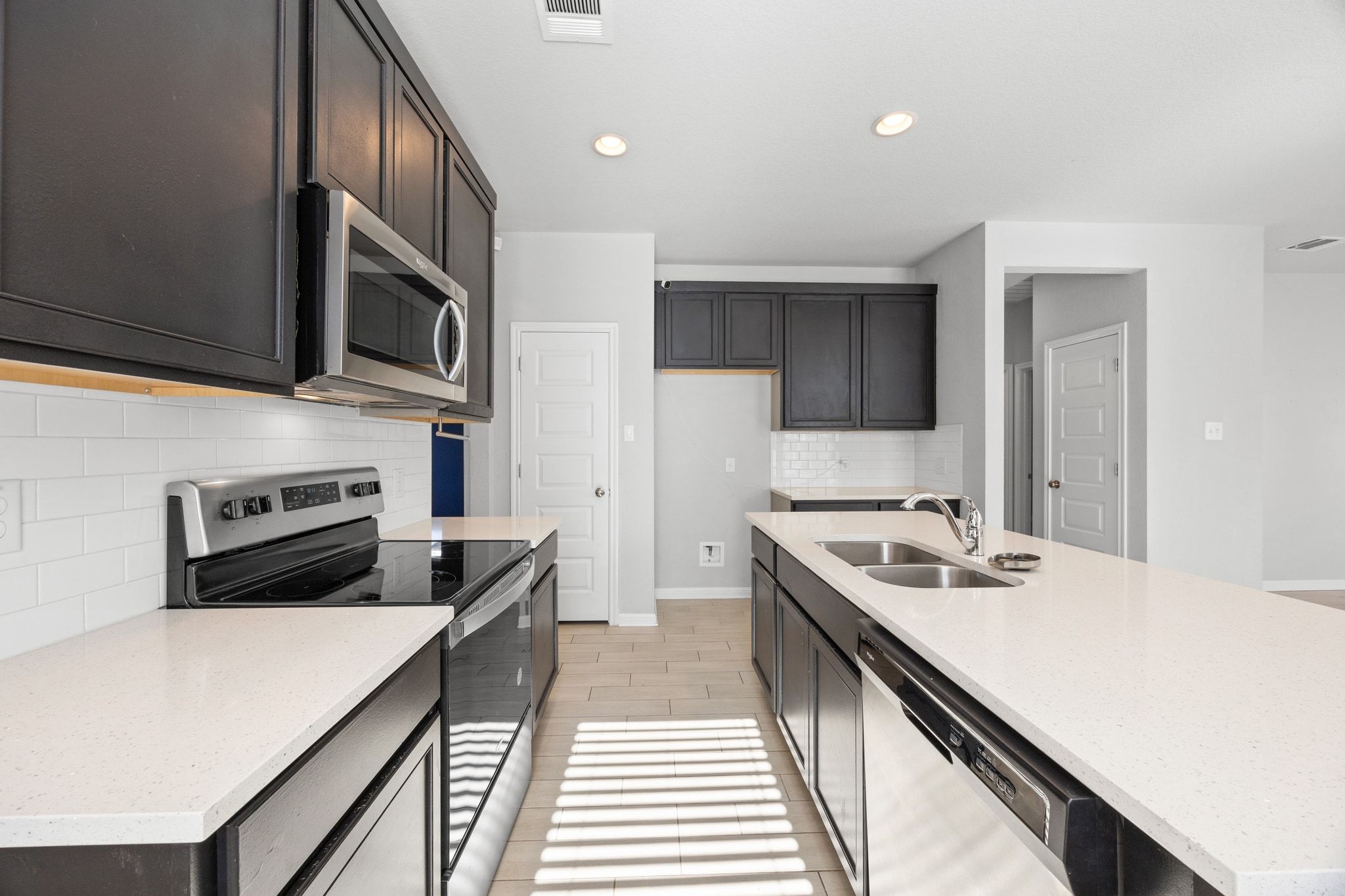 225 Unforgiven Lane Jarrell, TX 76537 - Photo 11 of 30 Kitchen featuring appliances with stainless steel finishes, light stone counters, tasteful backsplash, a kitchen island with sink, and recessed lighting