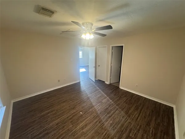 a view of an empty room with wooden floor and a ceiling fan