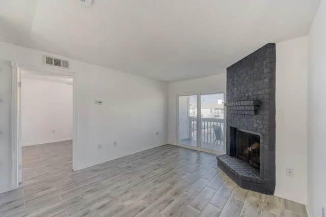 a view of an empty room with wooden floor fireplace and a window