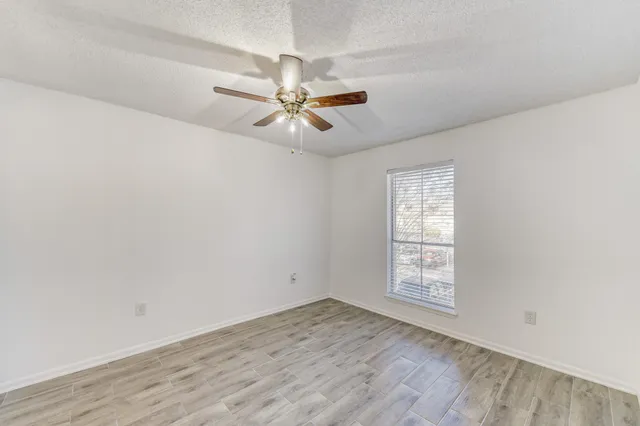 an empty room with wooden floor fan and windows