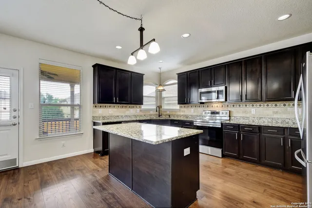 a kitchen with stainless steel appliances granite countertop wooden cabinets a sink dishwasher a stove and a refrigerator with wooden floor