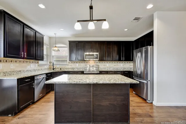 a kitchen with kitchen island granite countertop wooden cabinets and stainless steel appliances