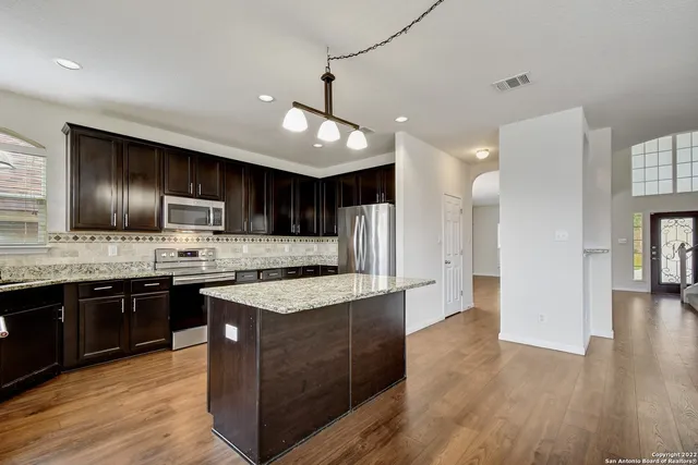 a kitchen with stainless steel appliances granite countertop wooden cabinets a refrigerator a stove a sink and a oven with wooden floor