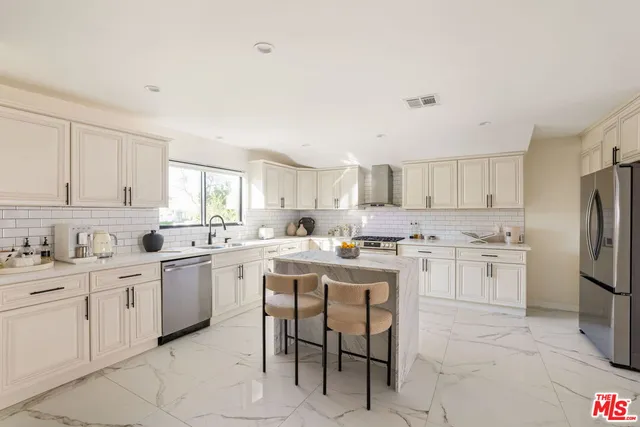 a kitchen with stainless steel appliances a sink a stove a refrigerator cabinets and a window