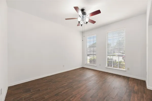 an empty room with wooden floor fan and windows