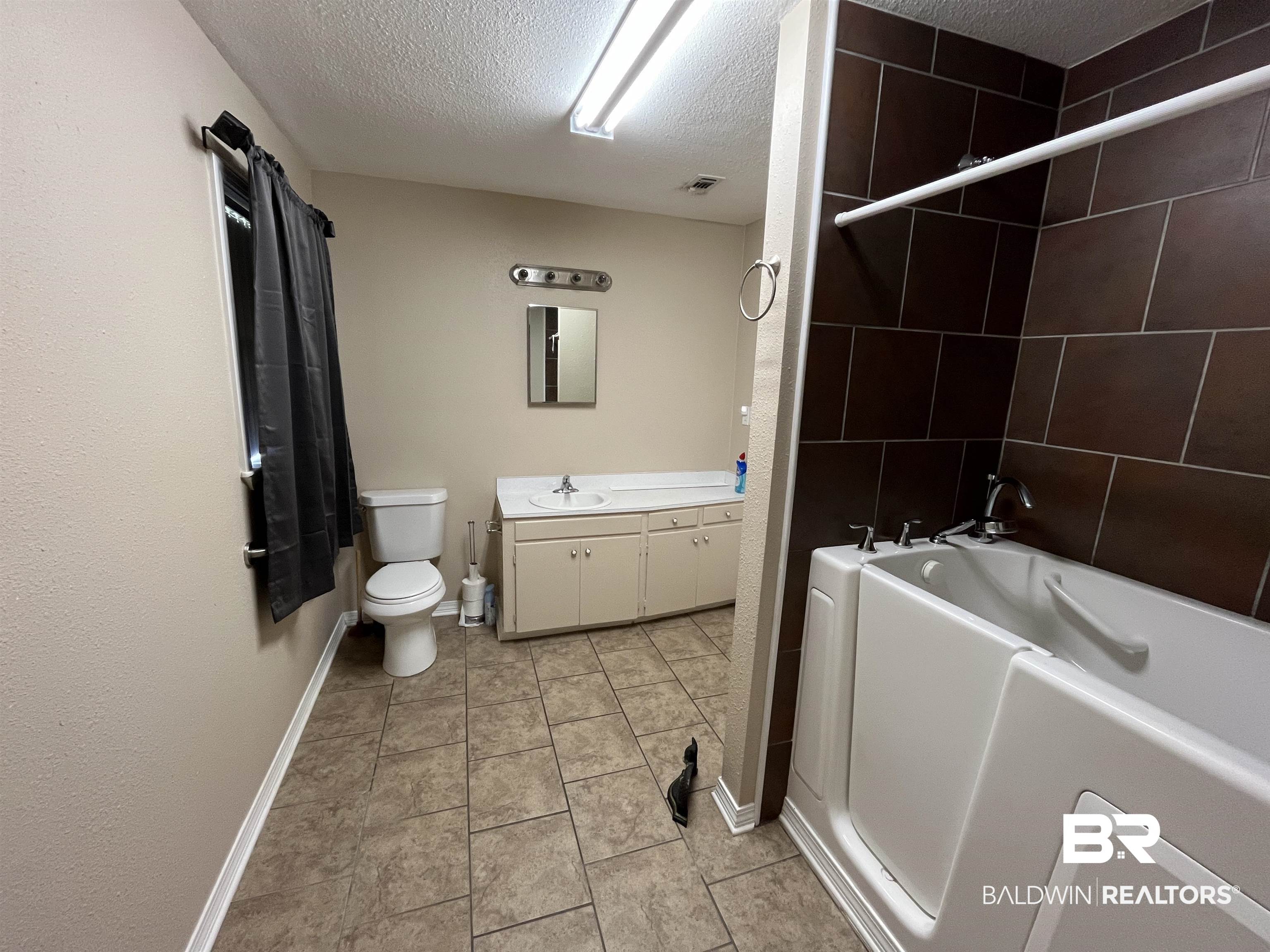1905 Rockaway Creek Road Atmore, AL 36502 - Photo 18 of 23 Bathroom featuring a walk-in tub, extensive brown tile surround, a single vanity with a white countertop and base cabinetry, and neutral-toned floor tiling