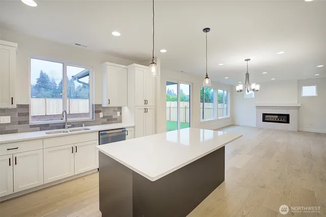 a large white kitchen with a stove a sink a center island and a wooden floor