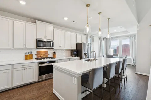 a kitchen with stainless steel appliances a stove a sink a refrigerator a center island a dining table and chairs