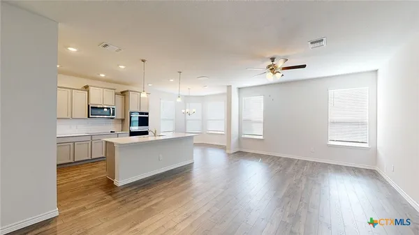 a view of an empty room and kitchen with wooden floor