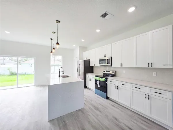 a large kitchen with stainless steel appliances granite countertop a stove top oven a sink a dining table and chairs with white cabinets