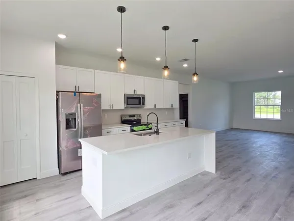 a large kitchen with kitchen island a refrigerator a stove a sink a center island a wooden floor and a view of living room