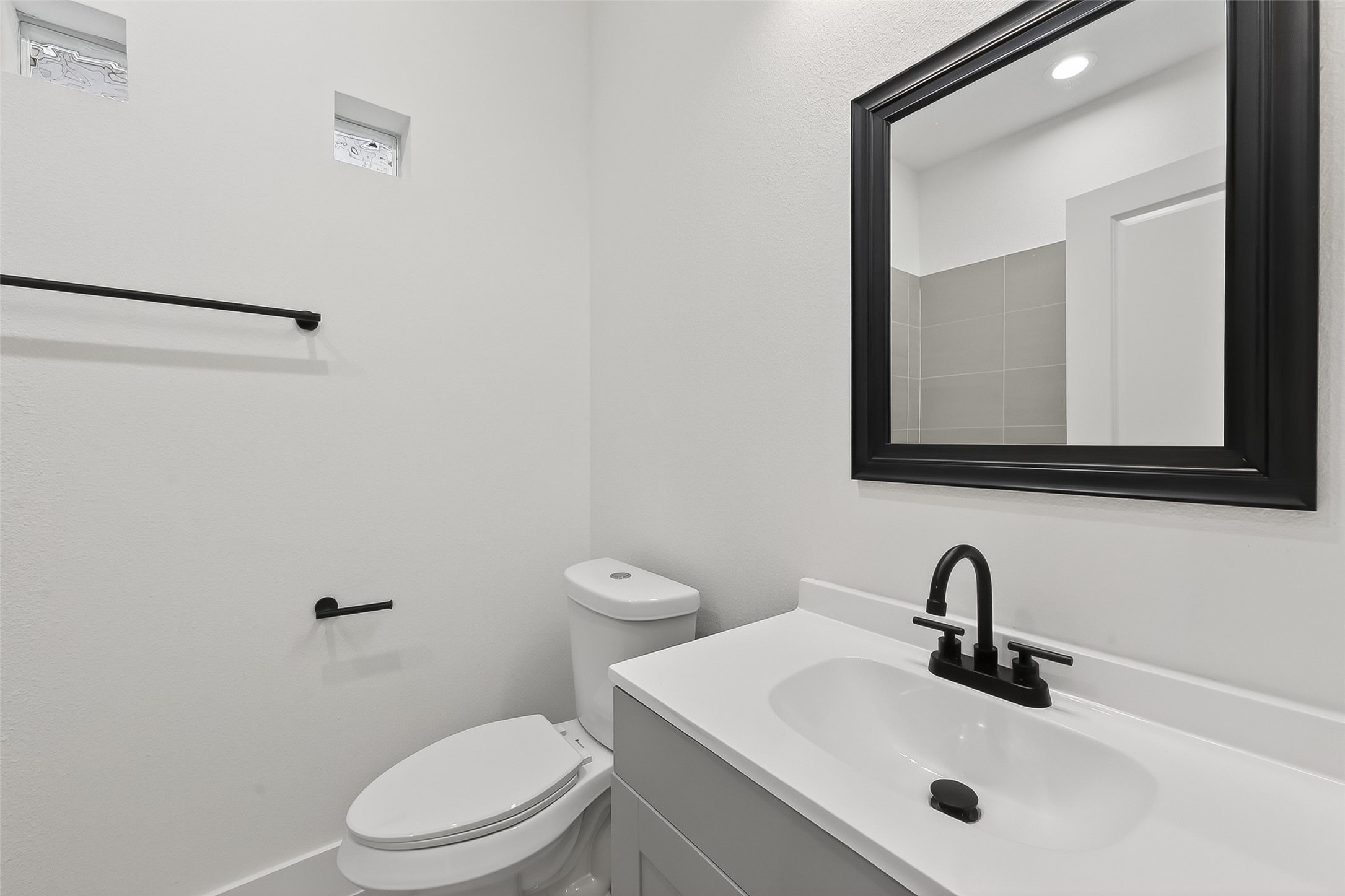 3514 Good Hope Street, Unit B Houston, TX 77021 - Photo 15 of 26 This is a modern bathroom featuring a sleek white vanity with a black framed mirror and matching black fixtures. The space is bright and minimalistic, with a small window providing natural light.
