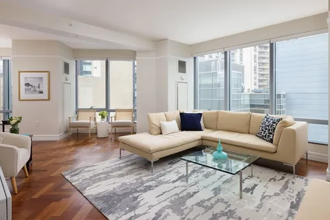 a living room with furniture large windows and wooden floor