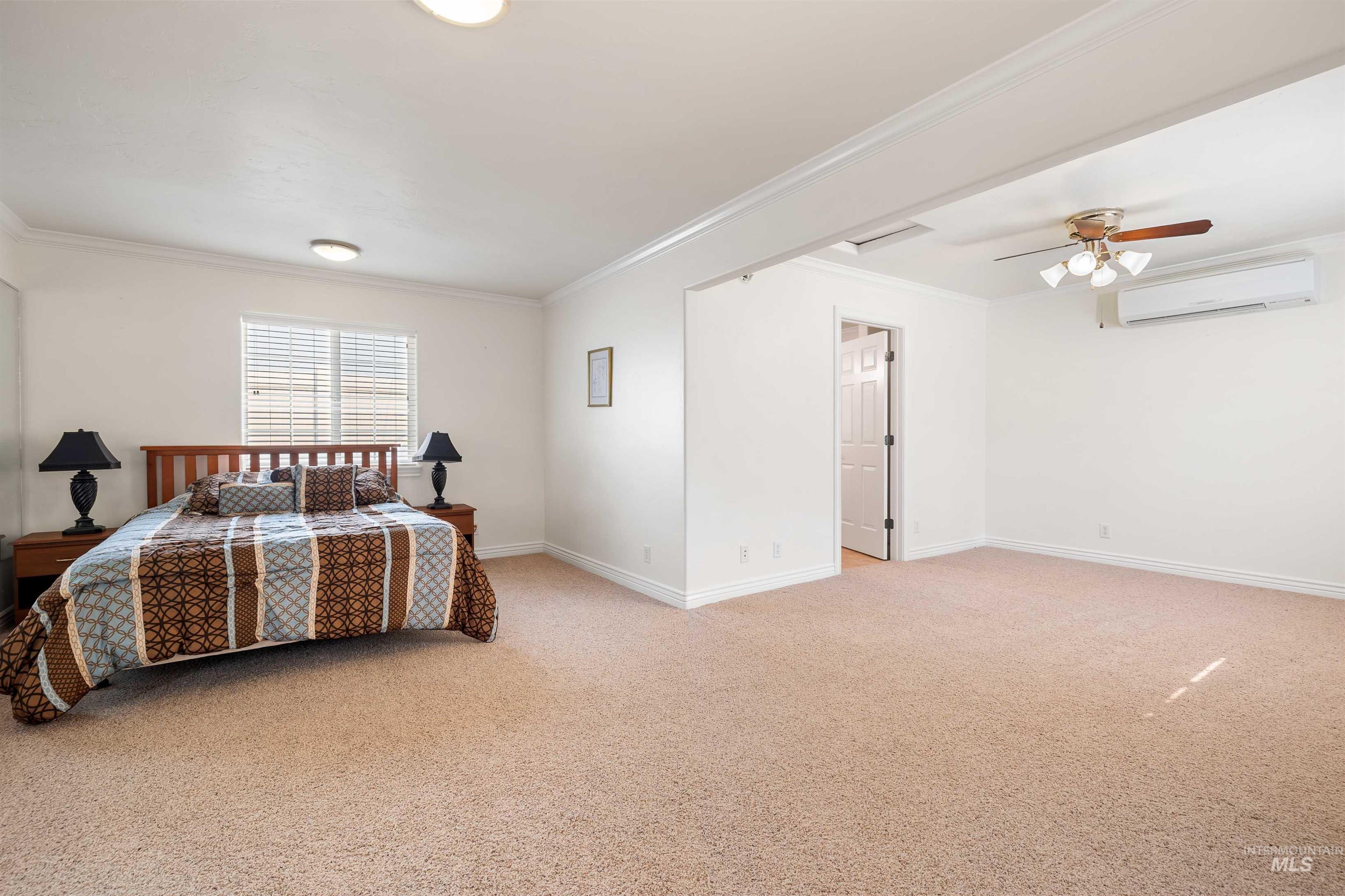 3404 Ridge Line Drive Kimberly, ID 83341 - Photo 41 of 50 Spacious room featuring neutral carpeting, white walls with crown molding, a large window with blinds, a ceiling fan, and a wall-mounted air conditioning unit