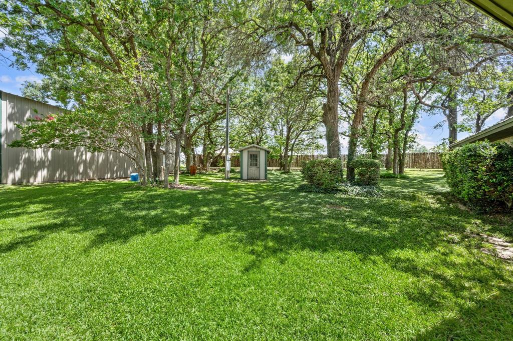 515 New Highland Road Springtown, TX 76082 - Photo 30 of 38 Expansive lawn area featuring numerous mature trees, a detached storage shed, perimeter fencing, and established shrubbery