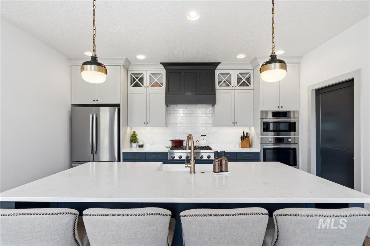 3794 South Single Tree Avenue Boise, ID 83716 - Photo 19 of 50 Spacious kitchen featuring a large white countertop island, stainless steel appliances, two-tone cabinetry, subway tile backsplash, and recessed lighting