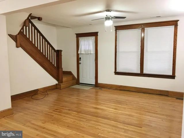 a view of an empty room with wooden floor and fan