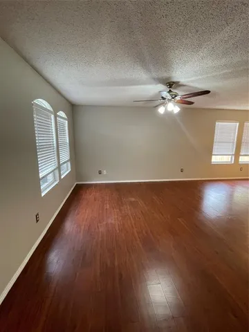 an empty room with wooden floor chandelier fan and windows
