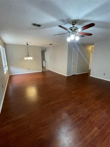a view of an empty room with wooden floor and a ceiling fan
