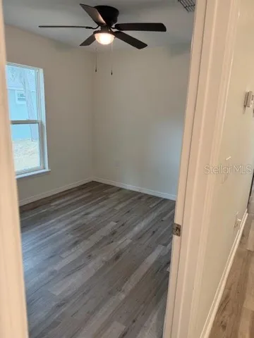 an empty room with wooden floor fan and windows