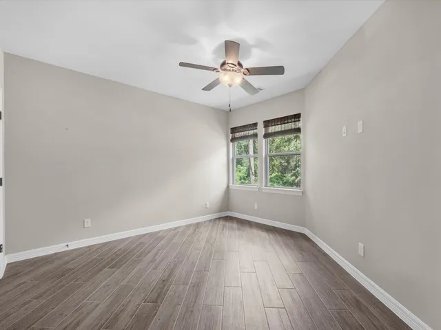 an empty room with wooden floor fan and windows