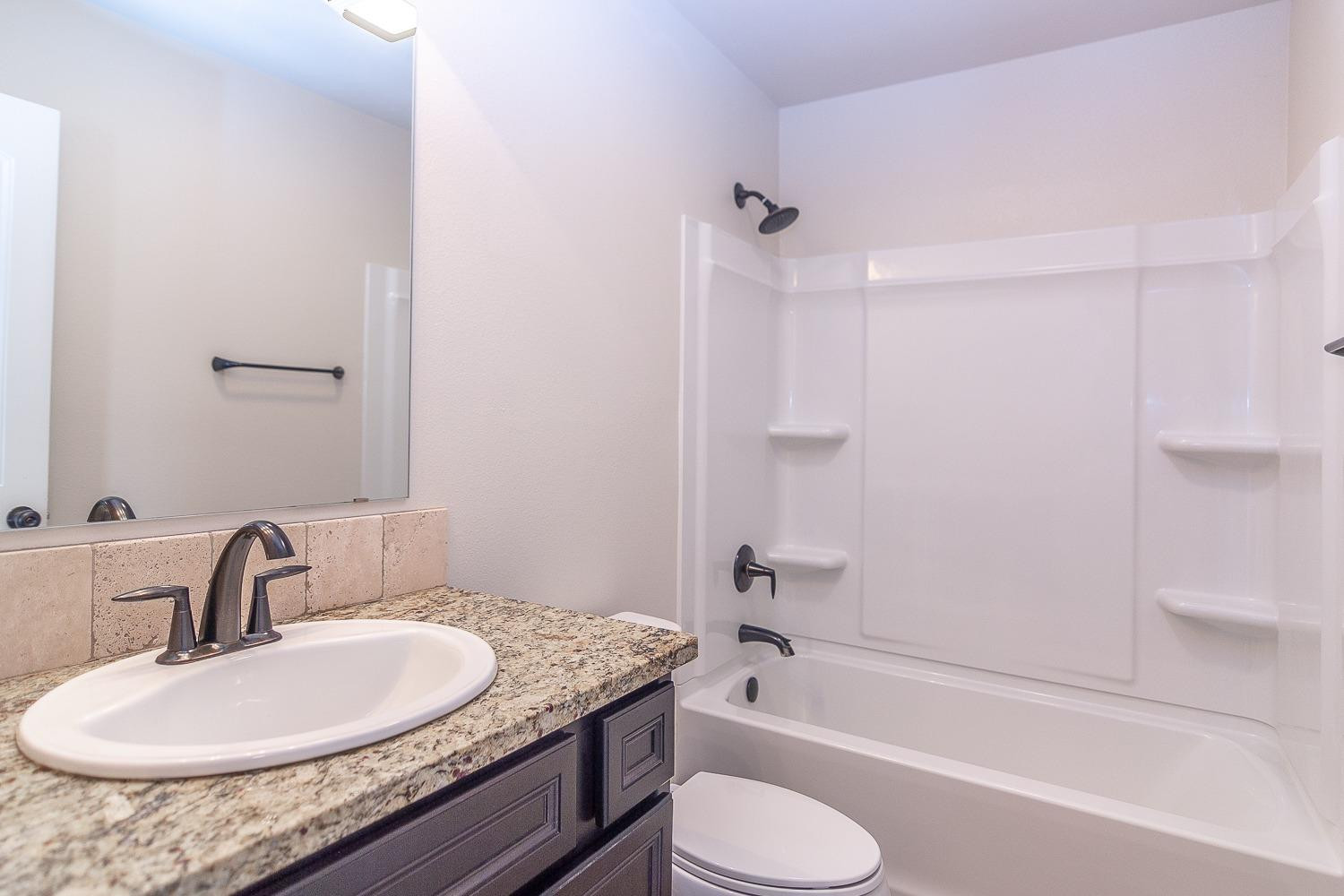7449 104th Street Lubbock, TX 79424 - Photo 15 of 16 a bathroom with a granite countertop sink toilet and shower