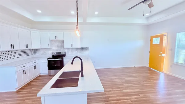 a kitchen with granite countertop a stove a sink and white cabinets with wooden floor