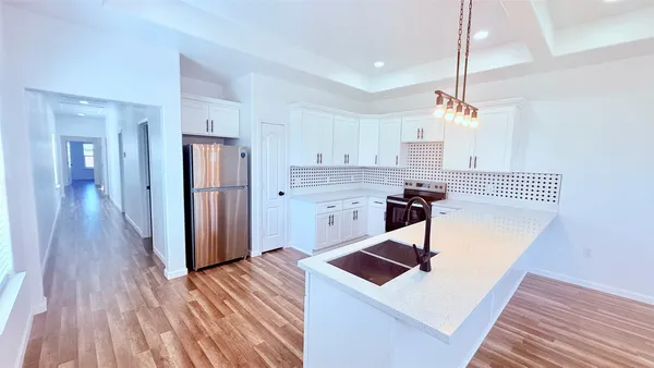 a kitchen with stainless steel appliances granite countertop a refrigerator a sink dishwasher a stove and white countertops with wooden floor