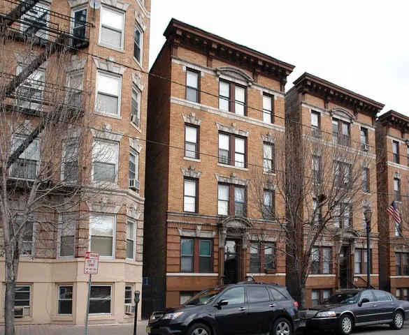 a front view of a building with lot of cars and trees