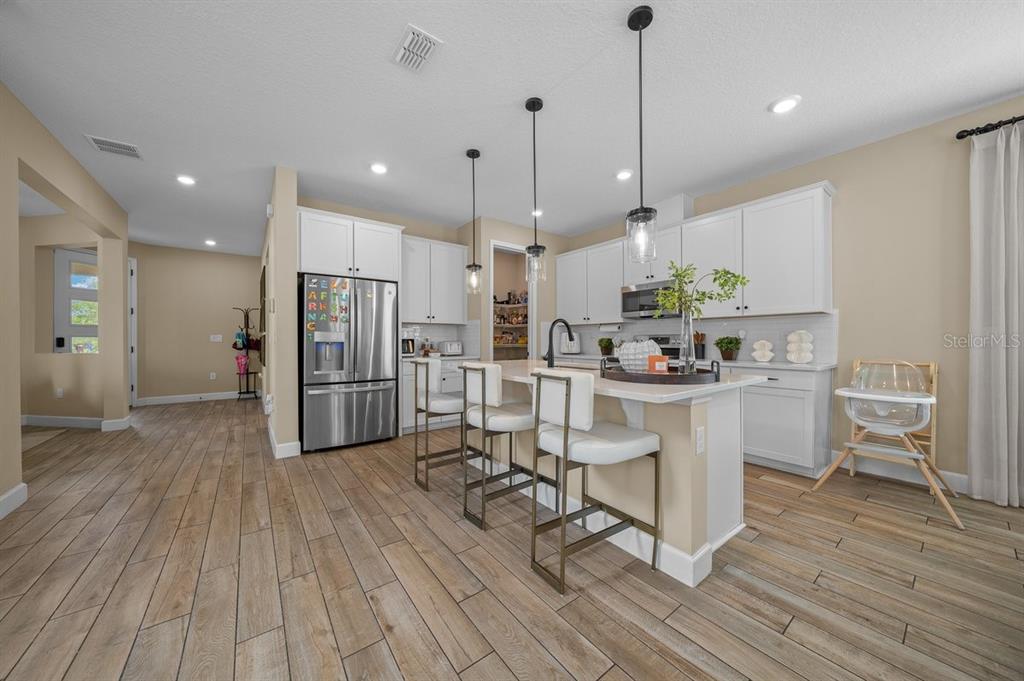 3916 Southern Vista Loop St. Cloud, FL 34772 - Photo 8 of 52 a kitchen with stainless steel appliances kitchen island granite countertop a refrigerator a oven a white stove a sink and white cabinets with wooden floor