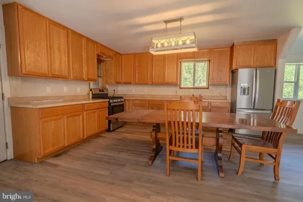 a open kitchen with stainless steel appliances granite countertop a stove top oven a refrigerator a dining table and chairs with wooden floor