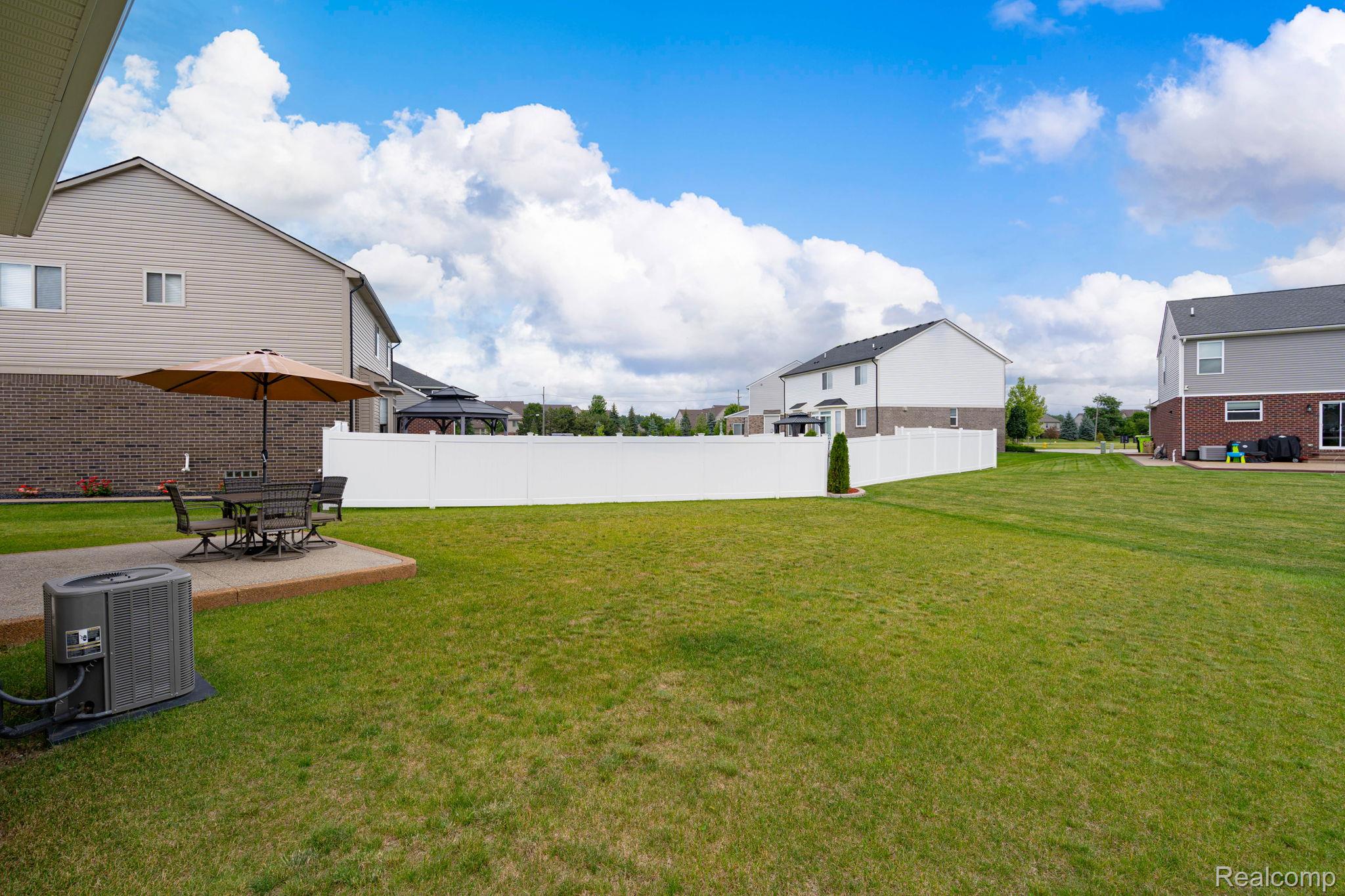 48904 Carnegie Way Macomb, MI 48042 - Photo 6 of 34 Expansive green lawn with a white vinyl fence and concrete patio
