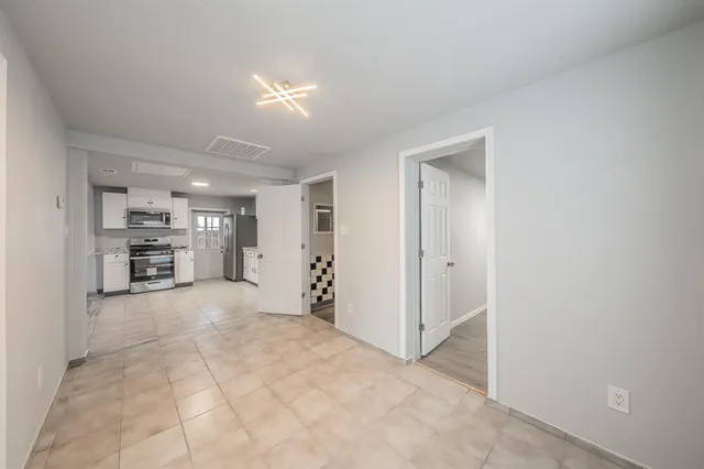 a view of an empty room with kitchen and window