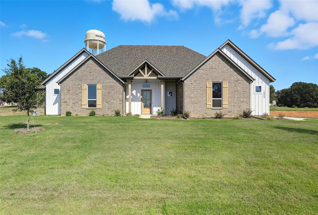View of front of house with board and batten siding, a front yard, brick siding, and covered porch