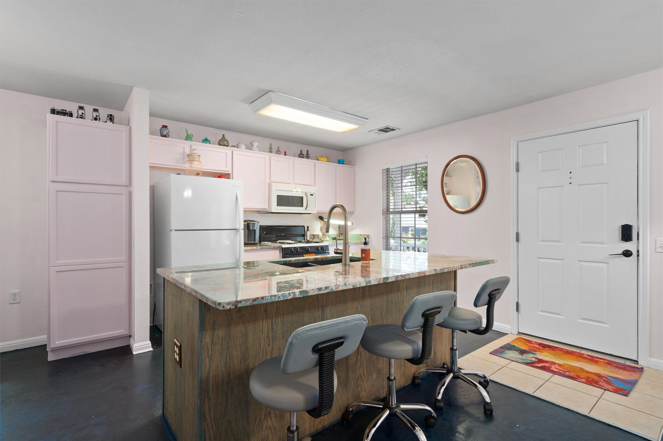 1407 Sanchez Street Austin, TX 78702 - Photo 8 of 34 Kitchen featuring a kitchen bar, light stone counters, a center island with sink, white appliances, and white cabinetry