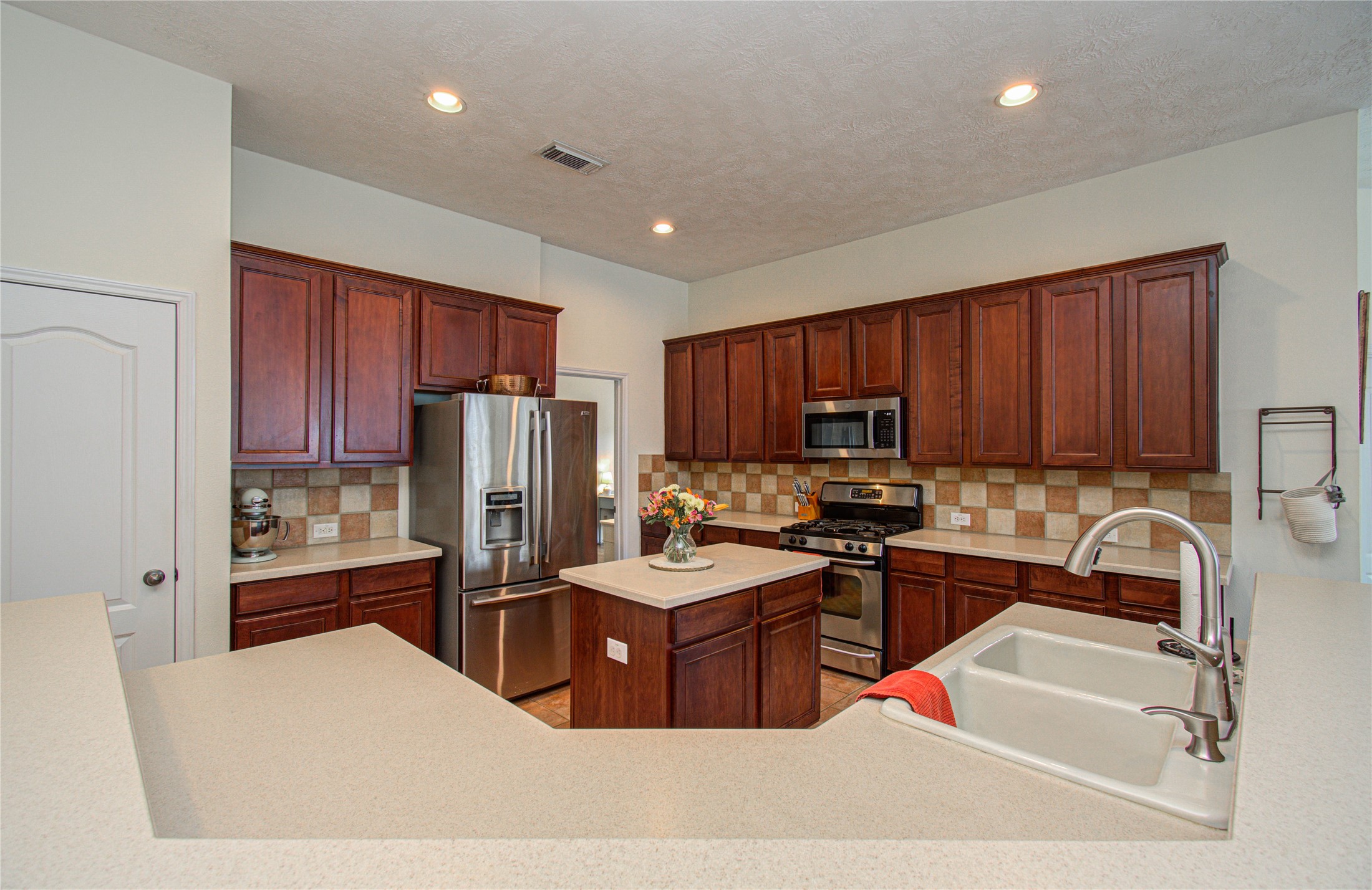 20007 Alcea Court Spring, TX 77379 - Photo 13 of 36 This kitchen features dark wood cabinetry, stainless steel appliances, a central island, and a dual sink. It offers ample counter space and a modern, warm ambiance.